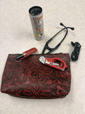 A red and black tooled leather pouch with floral patterns, shown with various accessories including a black stethoscope, a red-handled tool, a black device, and a can of Celera Energy drink on a light gray textured surface. Customer Photo 